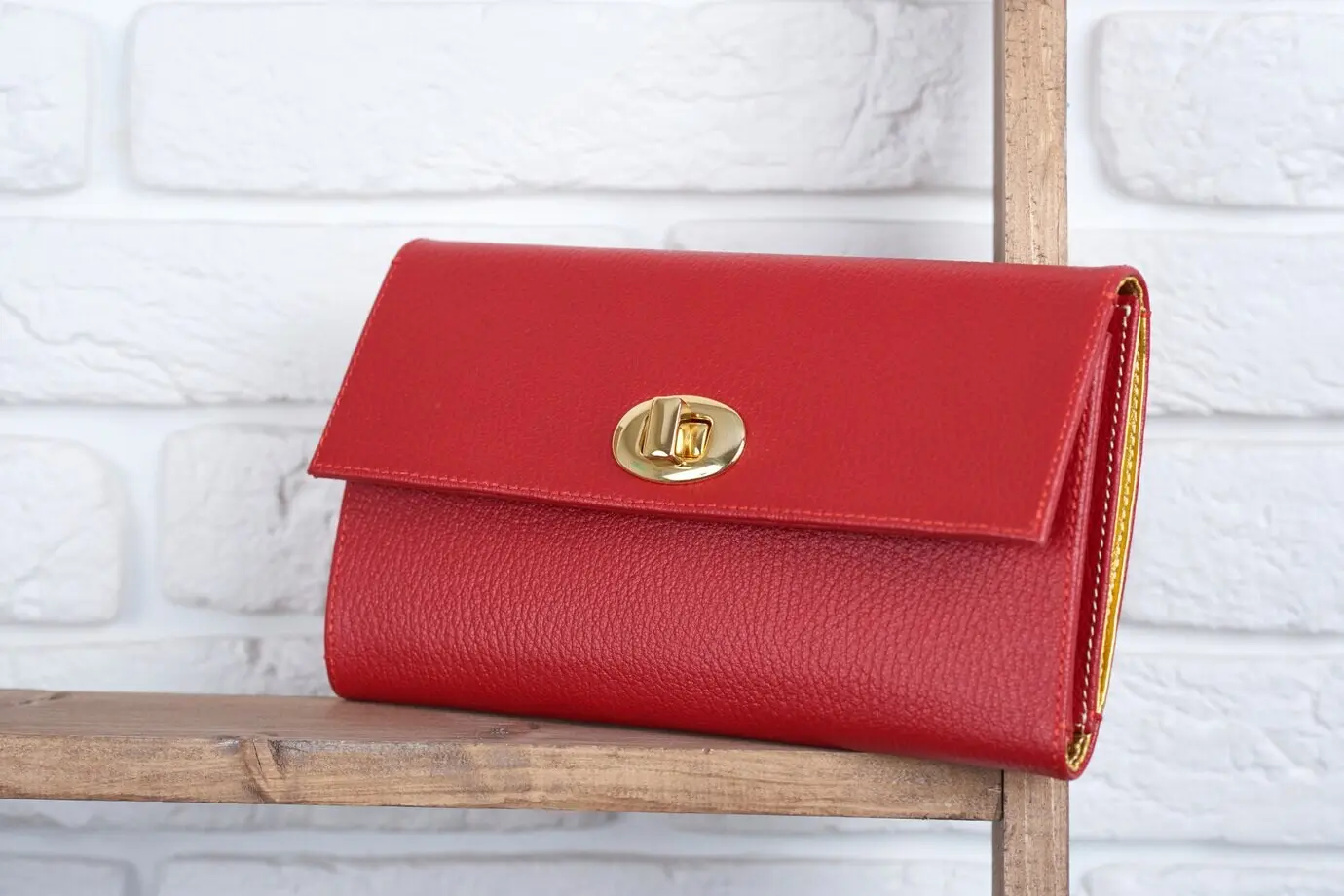 Rote Damen-Lederclutch liegt auf dem Holzregal an einer weißen Wand im Geschäft. Perfekt für einen lässigen Alltagslook und ein hübsches Cocktailkleid.